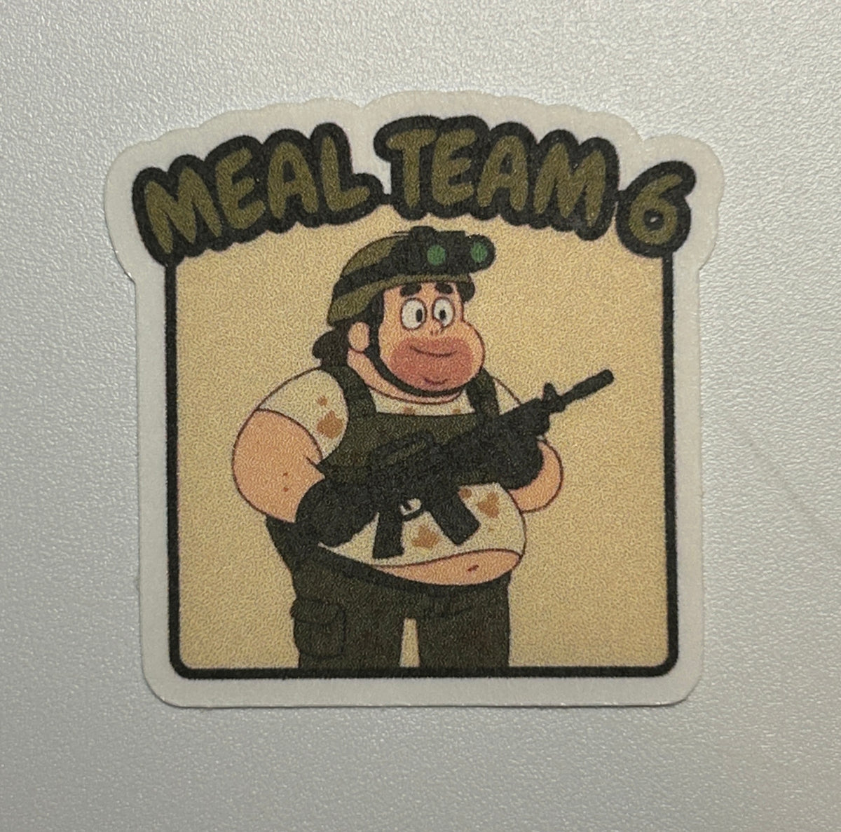 Sticker featuring a cartoon-style character holding a rifle, shown against a solid background with text above the illustration