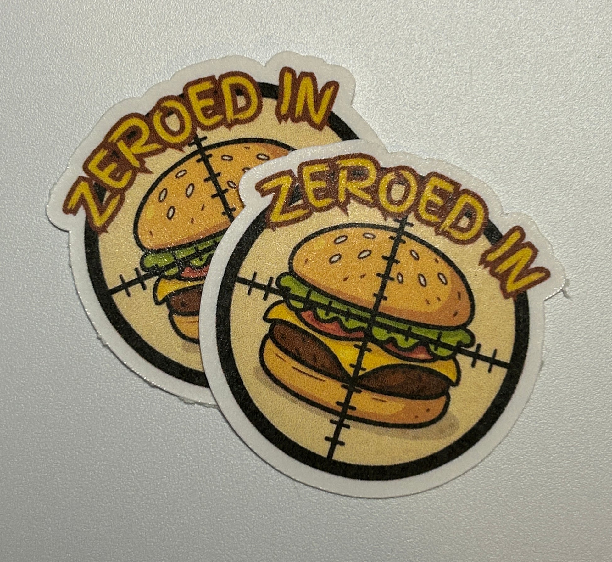 2 Round stickers showing an illustrated hamburger centered within a crosshair-style graphic and surrounding text.