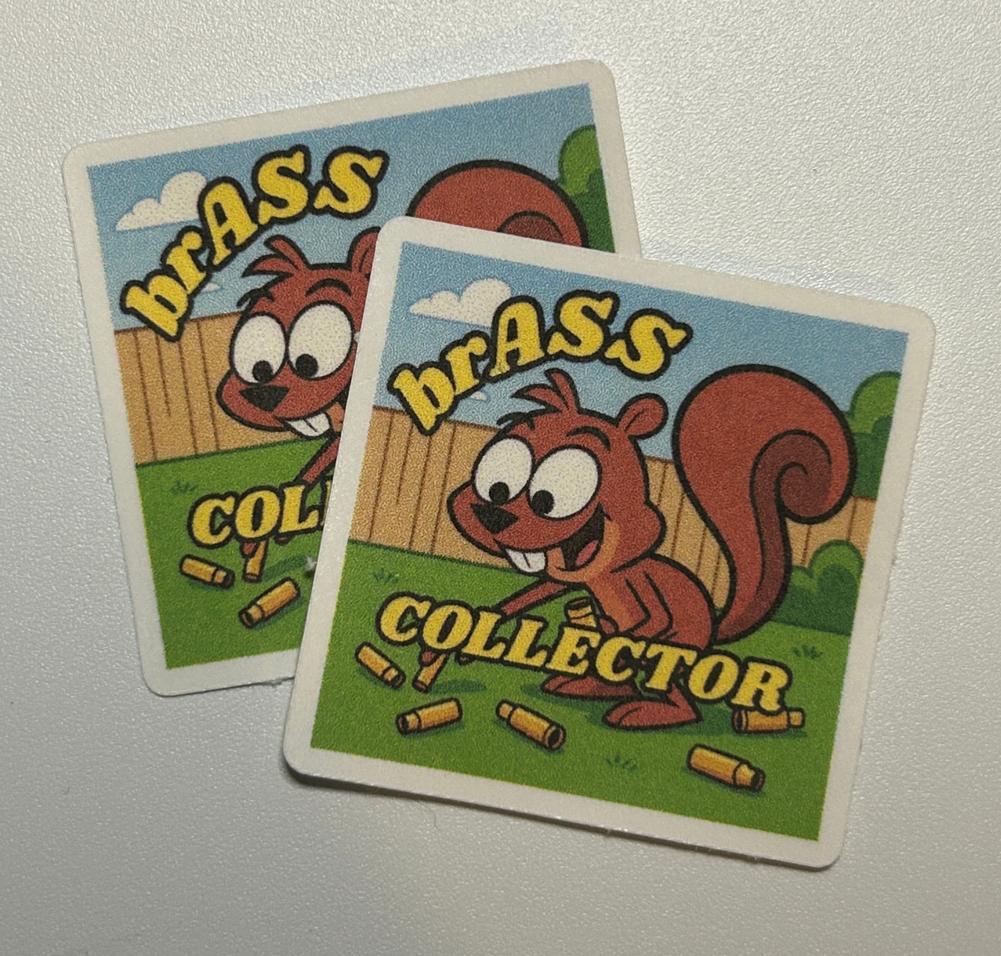 2 Square stickers featuring a cartoon-style squirrel illustration with text and small illustrated objects on a colorful background.