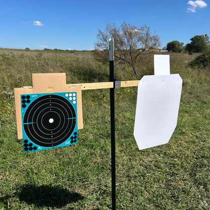 Two paper shooting targets mounted on horizontal wooden 2×2 boards attached to a vertical metal T-post using a black T-Dapter bracket, shown outdoors in a grassy field.